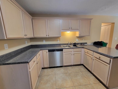Kitchen with dishwasher, a sink, a peninsula, a textured ceiling, and light tile patterned flooring