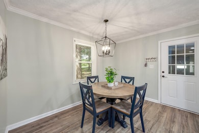 Dining area with wood finished floors, a textured ceiling, a chandelier, and crown molding