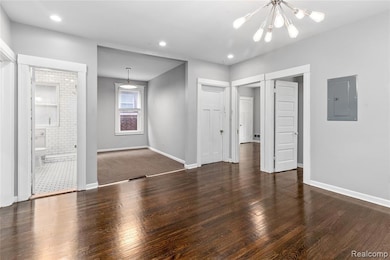 Unfurnished living room featuring dark wood-style floors, electric panel, a chandelier, and recessed lighting