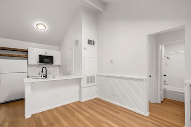 Kitchen featuring freestanding refrigerator, wainscoting, light wood-style floors, white cabinets, and a peninsula