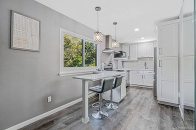 Kitchen with a breakfast bar, tasteful backsplash, hanging light fixtures, dark wood-type flooring, and wall chimney range hood