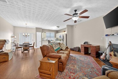 Living room featuring wood finished floors, a textured ceiling, ceiling fan, a fireplace, and a chandelier
