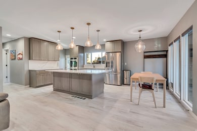 Kitchen with gray cabinetry, a center island, stainless steel fridge with ice dispenser, pendant lighting, and light wood-style floors