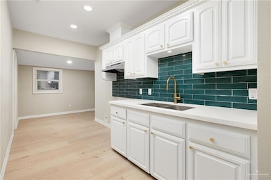 Kitchen with a sink, baseboards, tasteful backsplash, white cabinets, and light wood-type flooring
