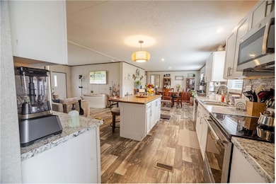 Kitchen featuring stainless steel appliances, white cabinets, a kitchen bar, hanging light fixtures, and light wood finished floors