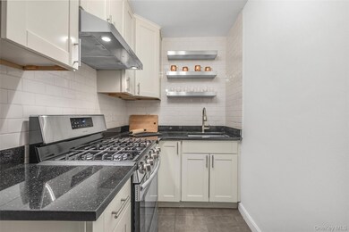 Kitchen featuring gas range, under cabinet range hood, dark stone countertops, backsplash, and open shelves