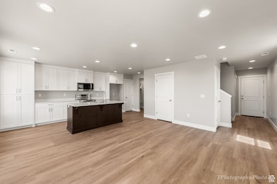 Kitchen with white cabinets, light wood-style flooring, appliances with stainless steel finishes, a kitchen island with sink, and recessed lighting
