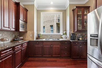 Kitchen with stainless steel appliances, reddish brown cabinets, dark stone counters, crown molding, and dark wood finished floors