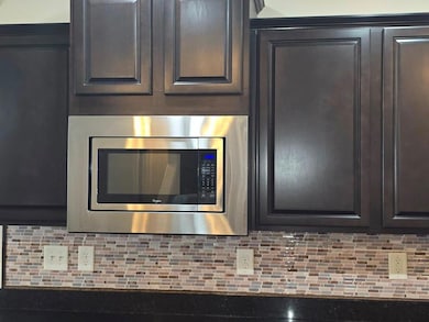 Kitchen view of stainless steel microwave, backsplash, and dark brown cabinets