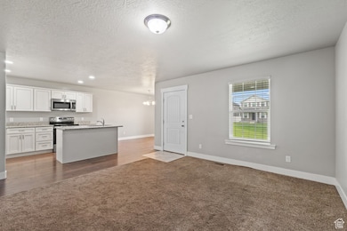 Kitchen with white cabinets, dark carpet, open floor plan, a chandelier, and appliances with stainless steel finishes