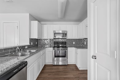 Kitchen with stainless steel appliances, white cabinets, light stone countertops, and tasteful backsplash