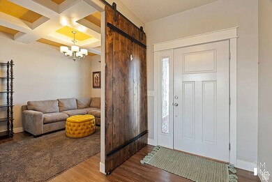 Entryway featuring coffered ceiling, a barn door, dark wood-type flooring, beamed ceiling, and a chandelier