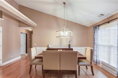 Dining space with vaulted ceiling, plenty of natural light, light wood-style flooring, and a wainscoted wall