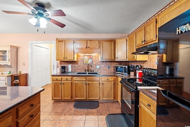 Kitchen featuring black appliances, under cabinet range hood, a sink, ceiling fan, and tasteful backsplash