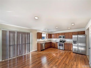 Kitchen with stainless steel appliances, light countertops, brown cabinetry, dark wood-type flooring, and recessed lighting
