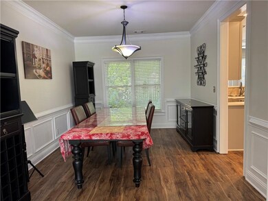 Dining space with a decorative wall, ornamental molding, dark wood-style floors, and wainscoting