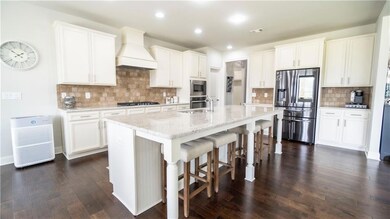 Kitchen featuring premium range hood, dark wood finished floors, stainless steel appliances, decorative backsplash, and a breakfast bar area