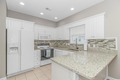 Kitchen with white appliances, a sink, a peninsula, white cabinets, and recessed lighting