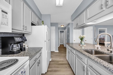 Kitchen featuring white appliances, a sink, light wood-type flooring, decorative backsplash, and a textured ceiling