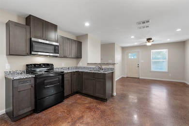 Kitchen with electric range, stainless steel microwave, finished concrete floors, light stone counters, and recessed lighting
