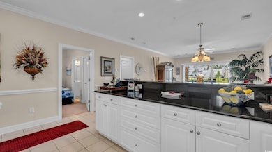 Kitchen featuring dark countertops, light tile patterned floors, crown molding, white cabinetry, and decorative light fixtures
