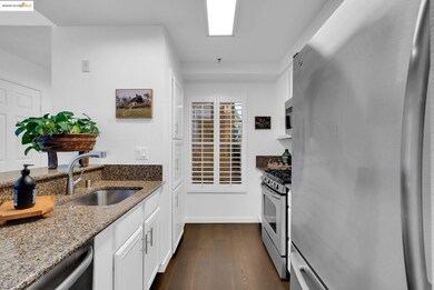 Kitchen with stainless steel appliances, white cabinets, dark stone counters, and dark wood-style floors