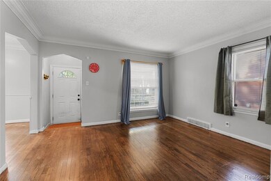 Foyer with ornamental molding, hardwood / wood-style flooring, a textured ceiling, plenty of natural light, and arched walkways