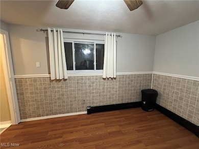 Unfurnished room featuring a wainscoted wall, tile walls, ceiling fan, a textured ceiling, and dark wood-style floors