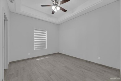 Empty room with a raised ceiling, light wood-type flooring, and ceiling fan