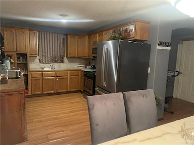 Kitchen featuring stainless steel appliances, light wood-style floors, light countertops, a textured ceiling, and brown cabinetry