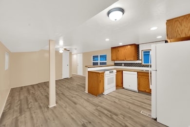 Kitchen featuring white appliances, a peninsula, brown cabinetry, open floor plan, and light wood-style floors