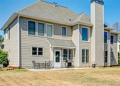 Back of property featuring a shingled roof, a yard, and a patio