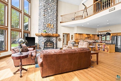 Living area with high vaulted ceiling, light wood-style floors, and a stone fireplace