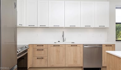 Kitchen featuring tasteful backsplash, white cabinets, appliances with stainless steel finishes, light countertops, and a sink