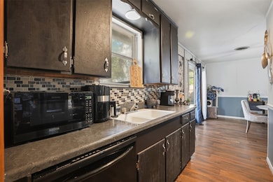 Kitchen with dark brown cabinets, black appliances, backsplash, dark wood-type flooring, and dark countertops
