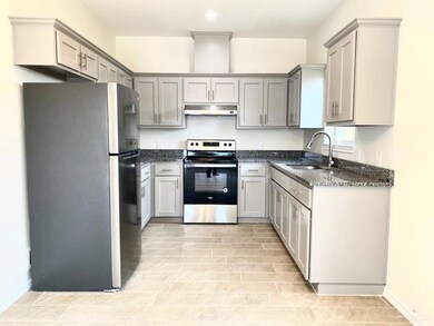 Kitchen featuring dark stone countertops, appliances with stainless steel finishes, gray cabinets, under cabinet range hood, and recessed lighting