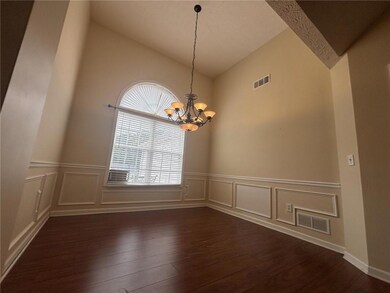 Spare room featuring vaulted ceiling, wood finished floors, a chandelier, a decorative wall, and wainscoting