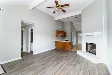Unfurnished living room featuring beam ceiling, ceiling fan, a fireplace, light wood-type flooring, and high vaulted ceiling