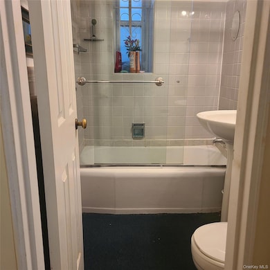 Bathroom featuring bath / shower combo with glass door and toilet