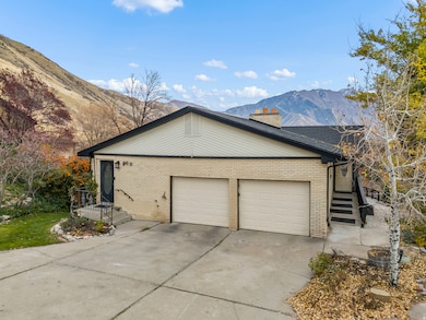 View of side of home with brick siding, driveway, a mountain view, a chimney, and an attached garage