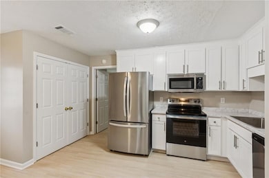 Kitchen featuring stainless steel appliances, white cabinetry, light wood-style flooring, a textured ceiling, and light stone countertops