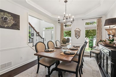 Dining room with plenty of natural light, crown molding, wood finished floors, a chandelier, and a tray ceiling