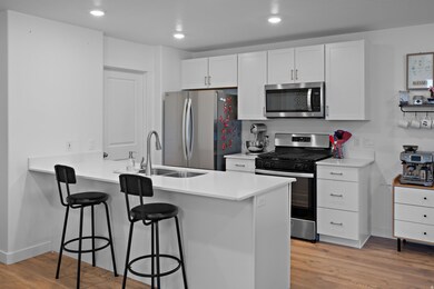 Kitchen with appliances with stainless steel finishes, a peninsula, a breakfast bar area, light wood finished floors, and white cabinetry