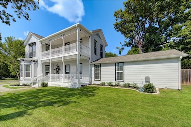 Back of house featuring a balcony, a porch, a yard