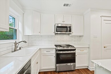 Kitchen with white cabinets, dark wood-type flooring, appliances with stainless steel finishes, and sink