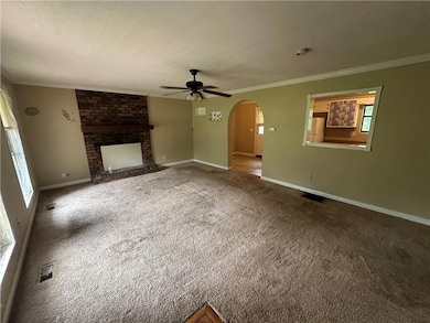 Unfurnished living room with ceiling fan, ornamental molding, arched walkways, a brick fireplace, and carpet