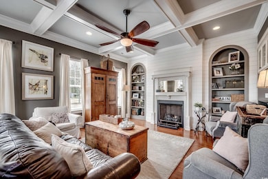 Living room with a fireplace, coffered ceiling, wood finished floors, and recessed lights.