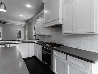 Kitchen with crown molding, dark countertops, backsplash, stainless steel appliances, and white cabinetry