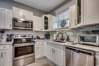 Kitchen featuring appliances with stainless steel finishes, glass insert cabinets, tasteful backsplash, and white cabinets