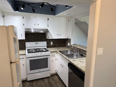 Kitchen with white appliances, a textured ceiling, backsplash, white cabinets, and light stone countertops